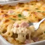 Gratin de pâtes au jambon facile et crémeux Gratin de pâtes au jambon et au fromage doré, avec une portion soulevée à la cuillère.